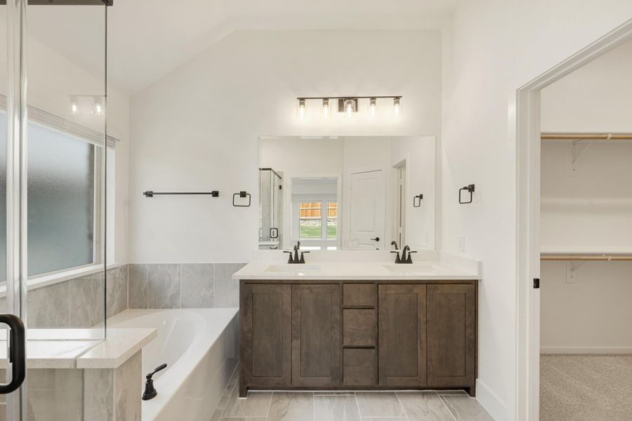 Master bathroom with double sink vanity, soaking tub, walk-in shower, and access to a walk-in closet