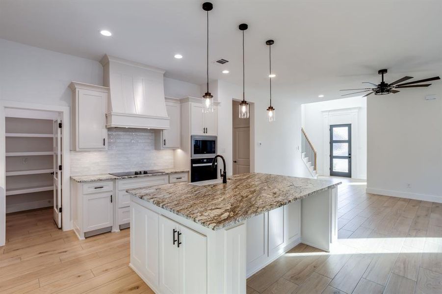 Kitchen featuring light wood finished floors, white cabinets, pendant lighting, and black appliances