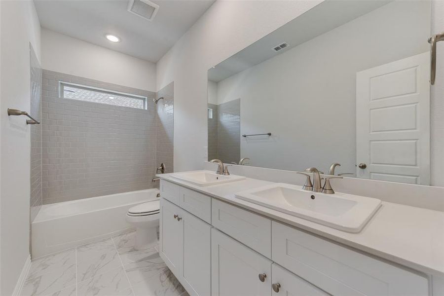 Full bathroom featuring toilet, tile patterned floors, tiled shower / bath, and double vanity