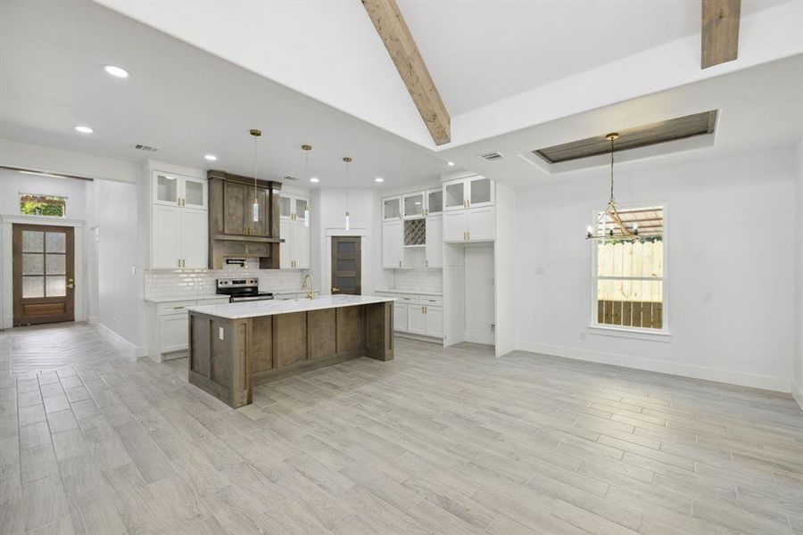 Kitchen featuring a spacious island, hanging light fixtures, electric range, white cabinets, and tasteful backsplash