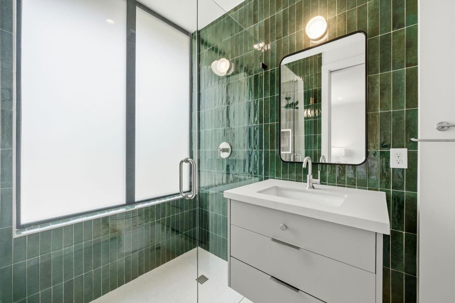 Green tiled walls and a sleek vanity create a vibrant, modern bathroom space.