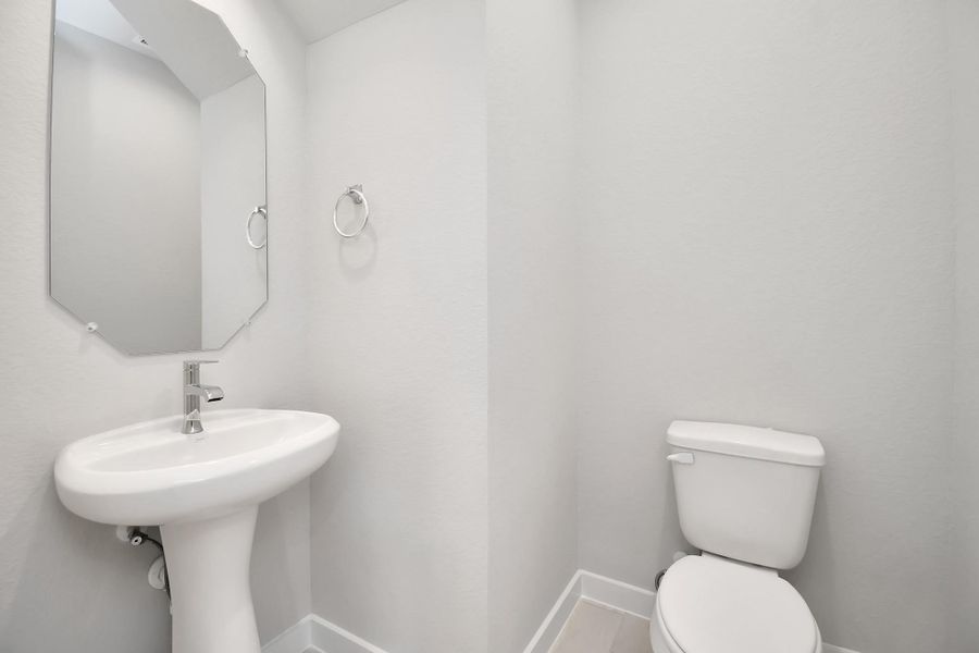 This half bathroom features a stylish pedestal sink, modern hardware, and bright recessed lighting, creating a sleek and inviting space. Sample photo of completed home with similar floor plan. Actual colors and selections may vary.