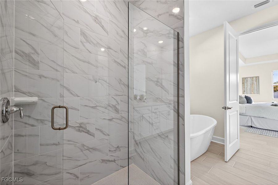 Ensuite bathroom featuring a freestanding bath, a marble finish shower, and wood tiled floors