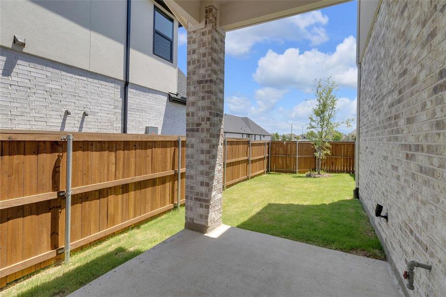 Covered patio with a brick column, concrete flooring, and an expansive lawn