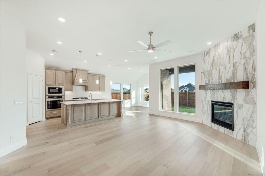Open-concept living area with hardwood floors, marble tile fireplace, and kitchen with large island and tan cabinets