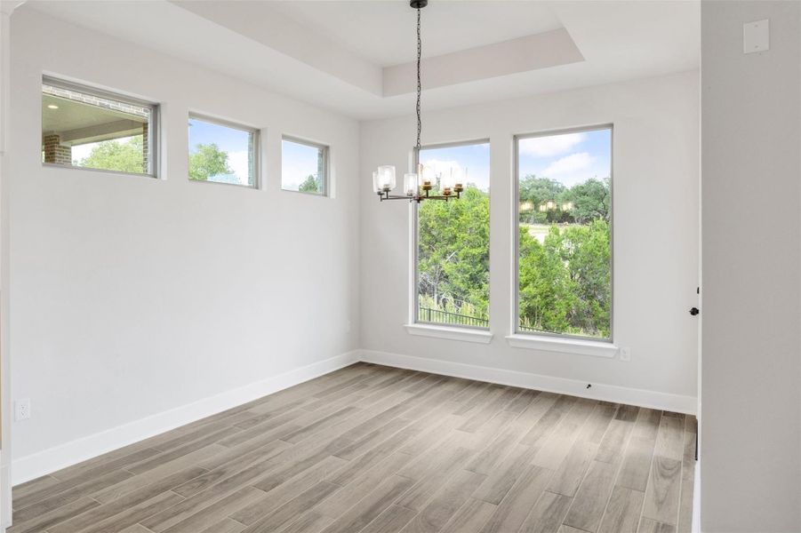 Unfurnished dining area featuring a tray ceiling, a chandelier, and light wood-style flooring Unfurnished dining area featuring a tray ceiling, a chandelier, and light wood-style flooring