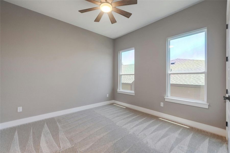 Bedroom featuring neutral wall paint, two windows with white trim, gray patterned carpet, and a ceiling fan with a light fixture