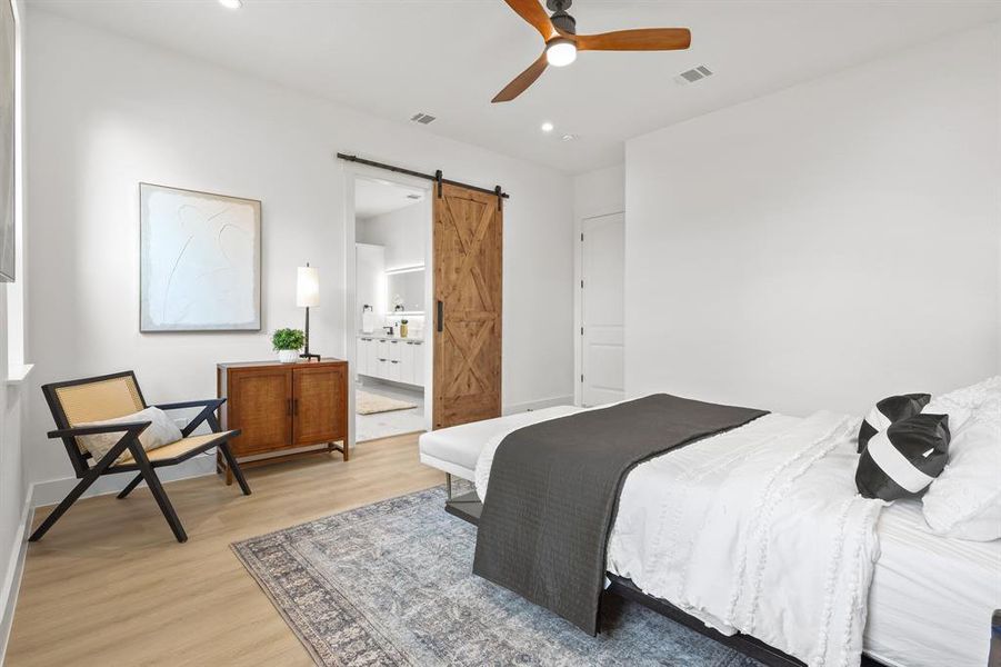 Bedroom with light hardwood / wood-style floors, a barn door, ceiling fan, and ensuite bath