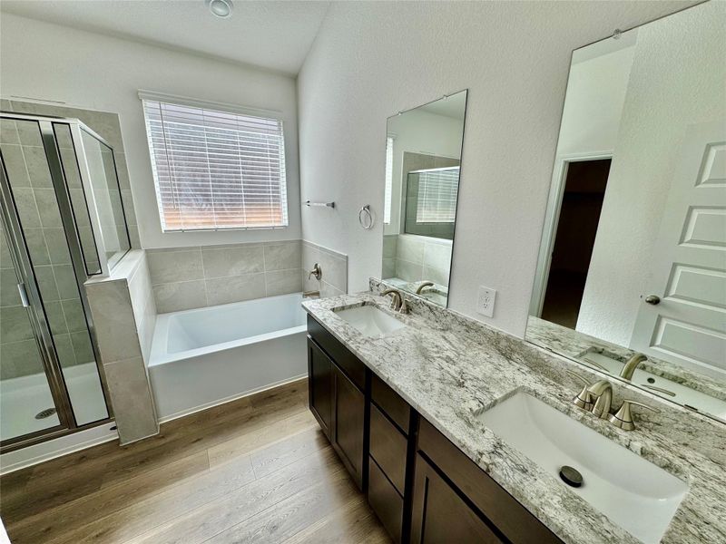 Full bath featuring light wood finished floors, a shower stall, a textured wall, double vanity, and a bath