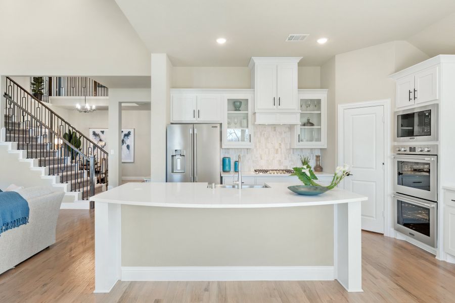 Open kitchen with white cabinets, large island, stainless appliances, and hardwood floors, open to staircase and living area Open kitchen with white cabinets, large island, stainless appliances, and hardwood floors, open to staircase and living area