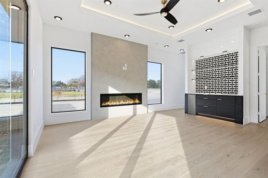 Same floorplan - different finishes. An open-concept living space features a linear electric fireplace set in a floor-to-ceiling stone surround alongside a built-in dry bar.