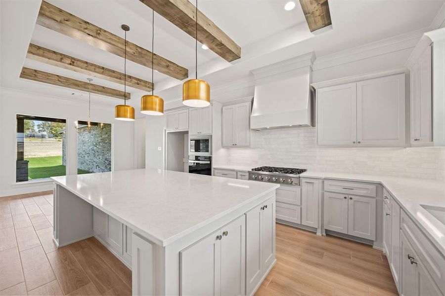 Kitchen with white cabinets, decorative backsplash, light wood-style floors, beamed ceiling, and decorative light fixtures Kitchen with white cabinets, decorative backsplash, light wood-style floors, beamed ceiling, and decorative light fixtures
