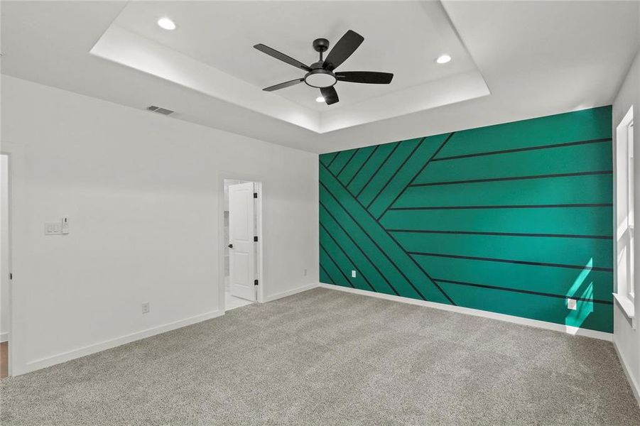 Carpeted empty room featuring ceiling fan and a tray ceiling