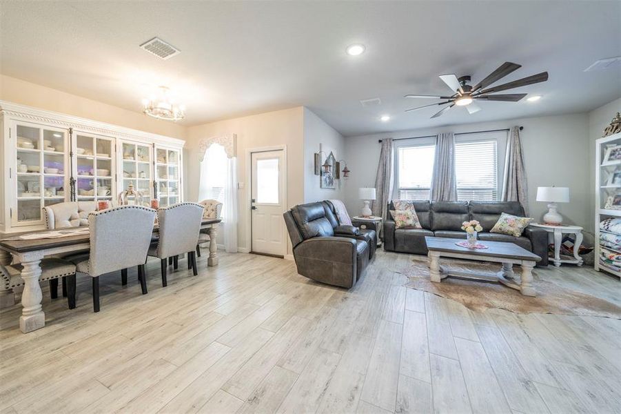 Living room with ceiling fan with notable chandelier and light hardwood / wood-style floors