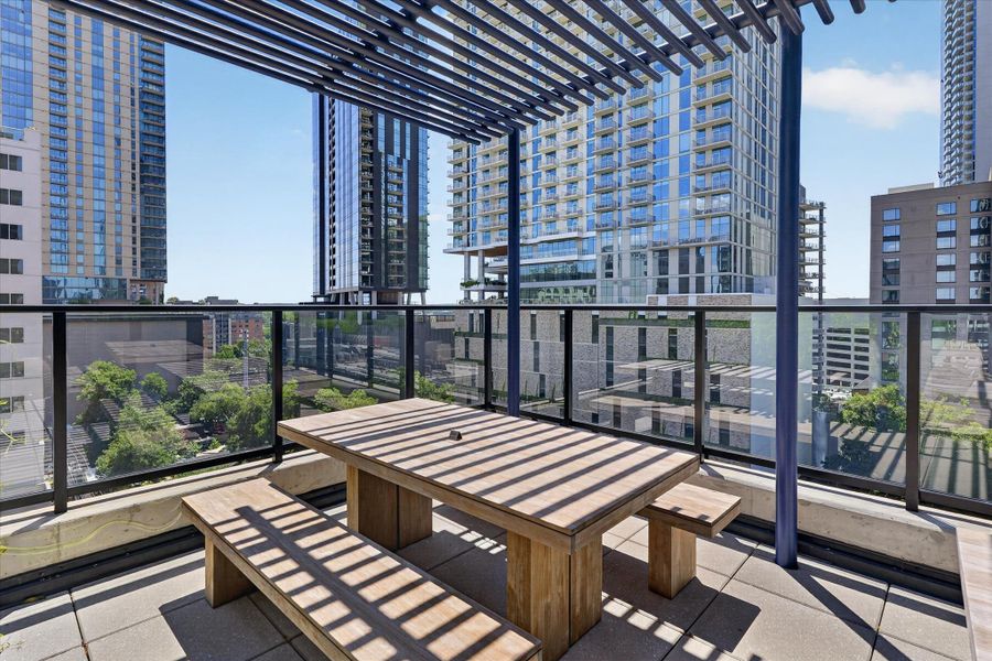 An inviting outdoor patio under a slatted pergola, ideal for urban dining amidst city tower views.