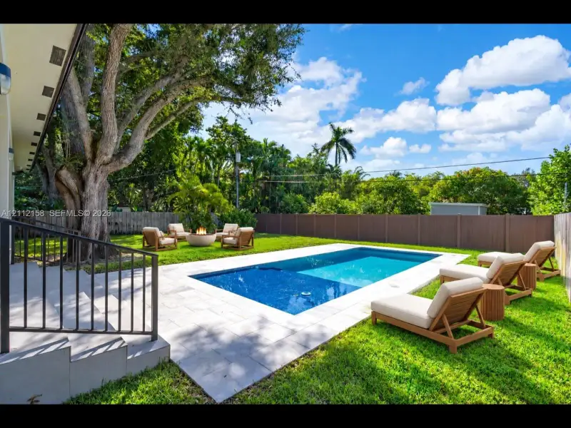 Your private backyard retreat: sparkling in-ground pool, light stone patio, lush lawn, and a fully fenced yard shaded by a mature tree