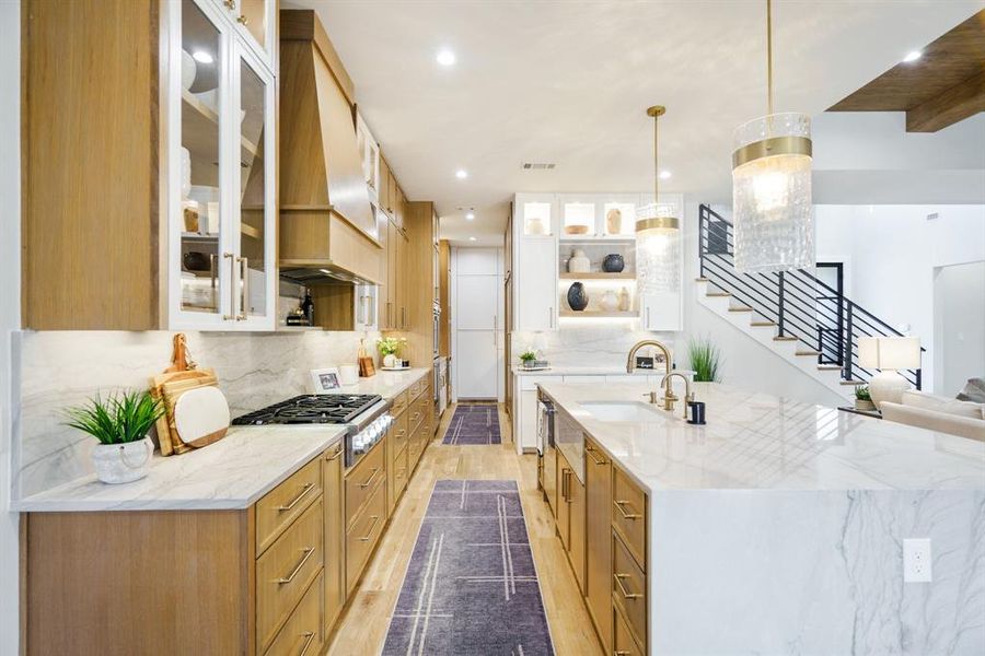 Kitchen with sink, premium range hood, hanging light fixtures, light stone countertops, and stainless steel gas stovetop