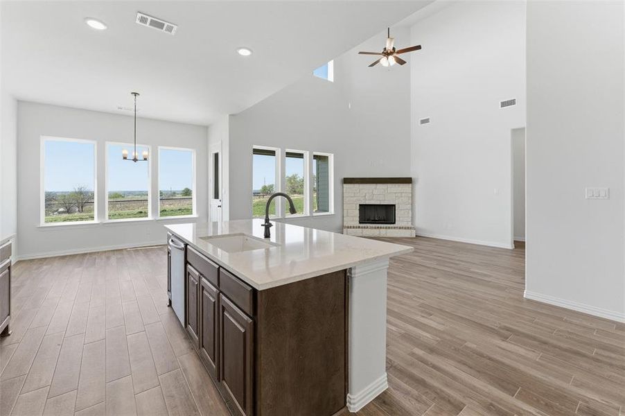 Kitchen featuring dark wood finish cabinets, wood tiled floors, an island with sink, a fireplace with raised hearth, and a high ceiling Kitchen featuring dark wood finish cabinets, wood tiled floors, an island with sink, a fireplace with raised hearth, and a high ceiling
