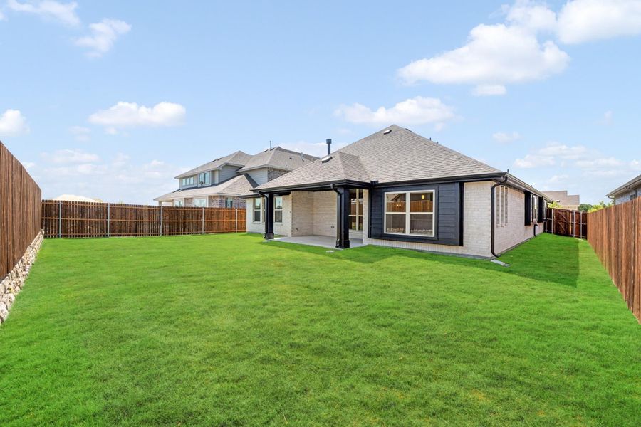 Backyard of single-story brick home with covered patio, large green lawn, and wood privacy fence