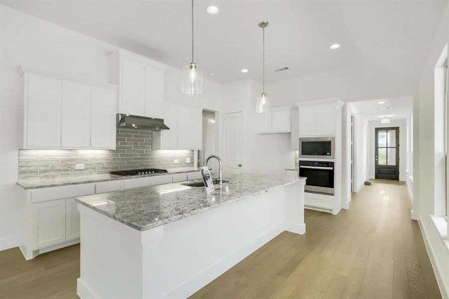 Contemporary kitchen featuring a large central island with a light-toned countertop, white cabinetry, integrated stainless steel appliances, a tile backsplash, and light wood-finish flooring