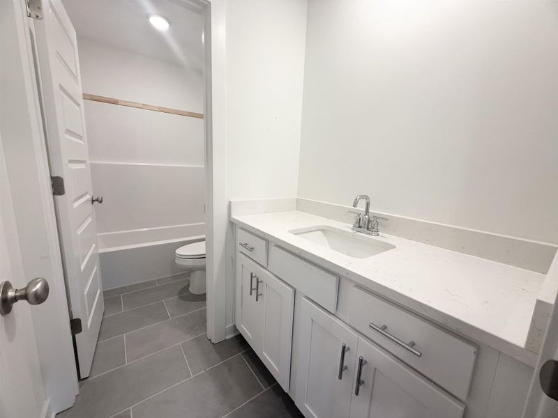 Bathroom vanity featuring white shaker cabinetry, brushed nickel hardware, and a light-toned countertop with an integrated sink Bathroom vanity featuring white shaker cabinetry, brushed nickel hardware, and a light-toned countertop with an integrated sink