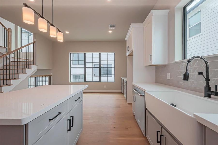 Experience modern elegance in this kitchen with sleek white and gray cabinetry, black handles, a gas stove, and a chic hexagonal tile backsplash. Quartz countertops and abundant natural light complete the sophisticated look.