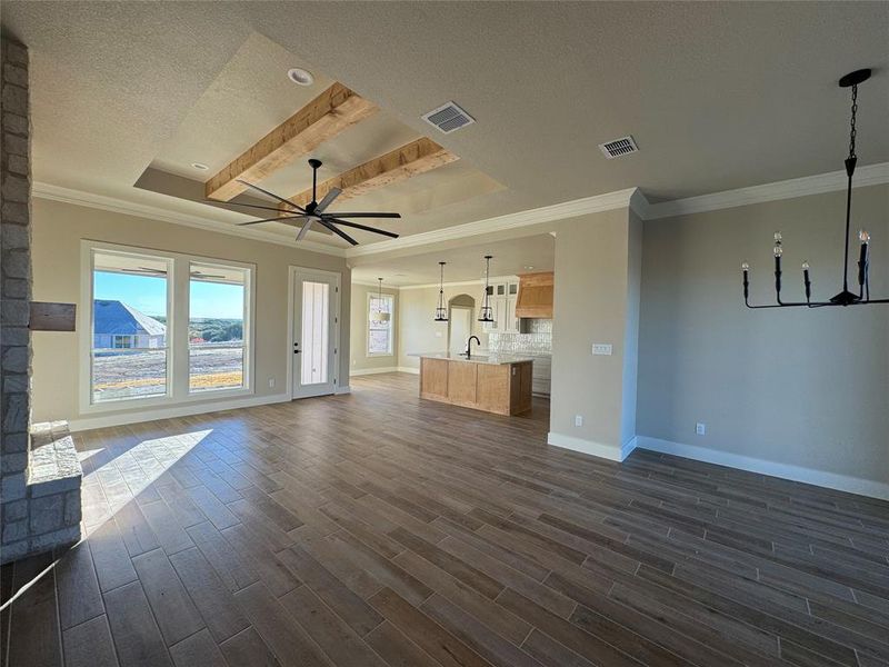 Unfurnished living room with dark wood-type flooring, a raised ceiling, crown molding, ceiling fan, and a textured ceiling