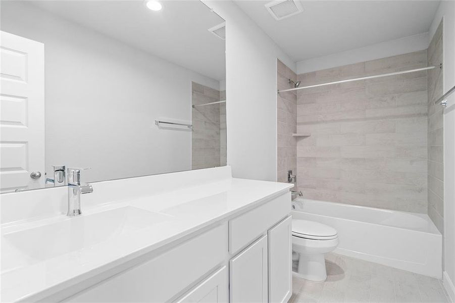 Secondary bath features tile flooring, bath/shower combo with tile surround, white stained wood cabinets, beautiful light countertops, mirror, sleek fixtures and modern finishes.