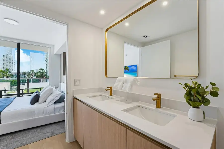Dual-sink vanity with light wood cabinetry, white countertops, integrated sinks, brass-toned hardware, and a large wall-mounted mirror