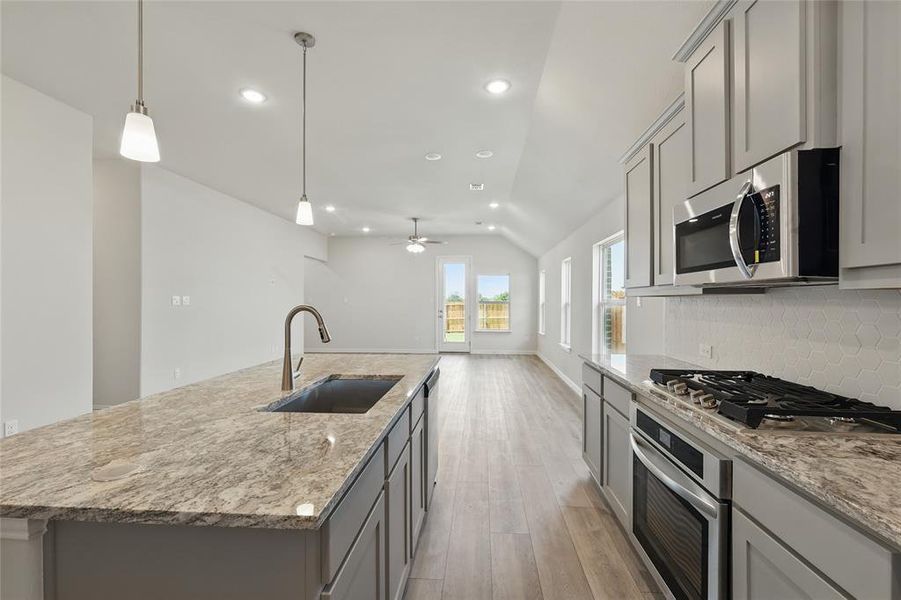 Kitchen with lofted ceiling, a kitchen island with sink, stainless steel appliances, gray cabinetry, and light stone counters