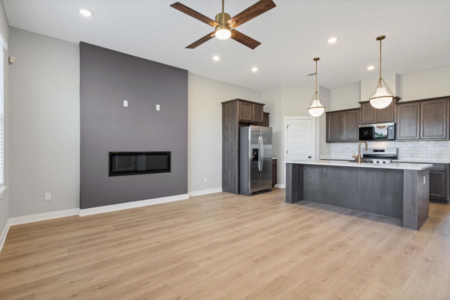 Open-concept living space featuring wood-finish flooring, a linear electric fireplace within a contrasting accent wall, and a kitchen island with pendant lighting