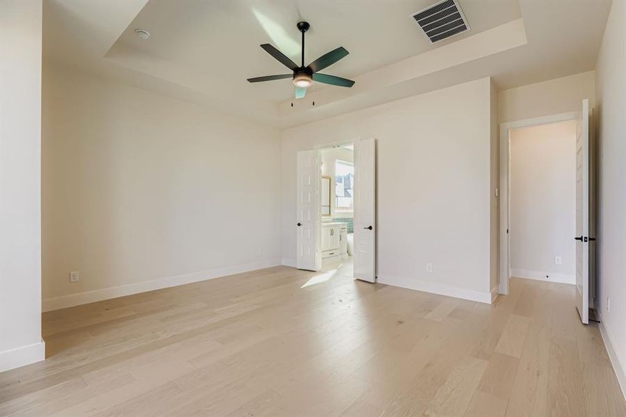 Empty room with a tray ceiling, light wood-type flooring, and ceiling fan