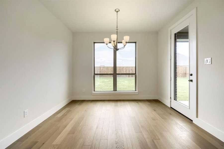 Spacious room featuring wood-finish flooring, a contemporary chandelier, a large window, a glass-paneled door, and clean white baseboards Spacious room featuring wood-finish flooring, a contemporary chandelier, a large window, a glass-paneled door, and clean white baseboards