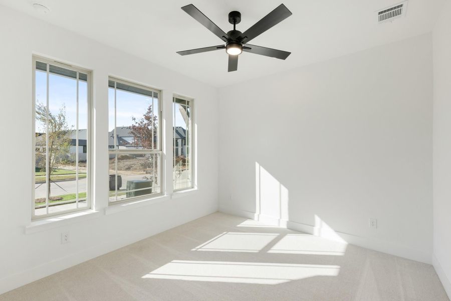 Empty bedroom with carpet flooring, black ceiling fan, and three large windows with neighborhood views