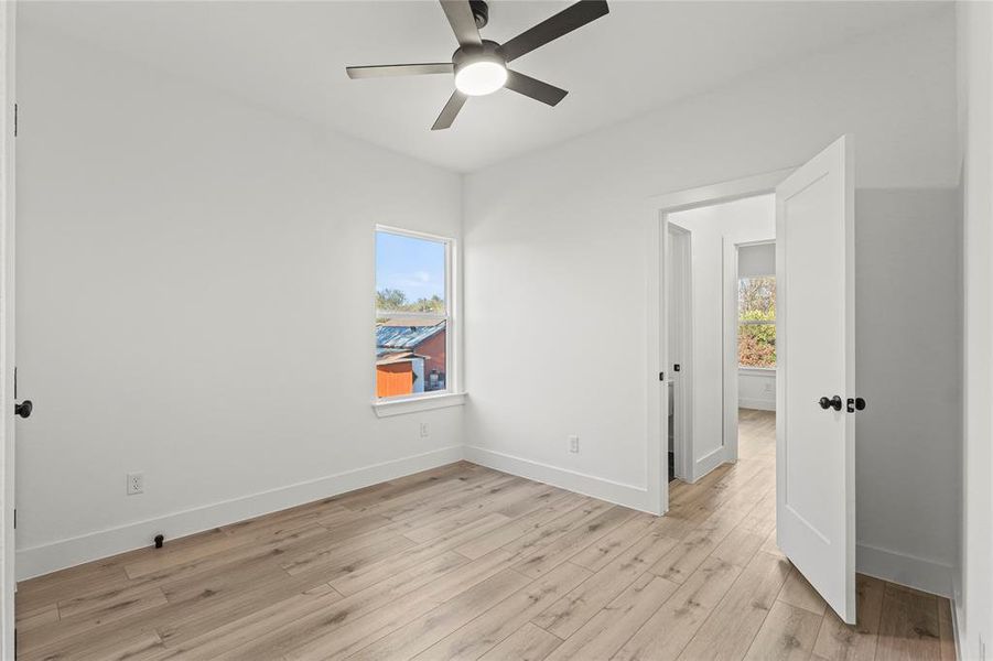 Unfurnished bedroom featuring light wood-style floors, multiple windows, and a ceiling fan