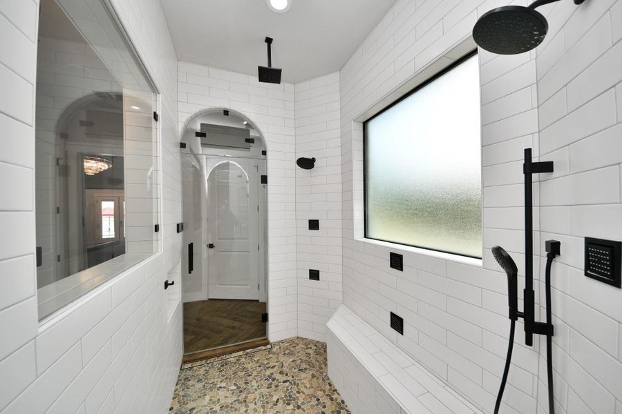 Experience luxury in this sleek, modern shower featuring elegant white subway tiles, matte black fixtures, and a pebbled floor.