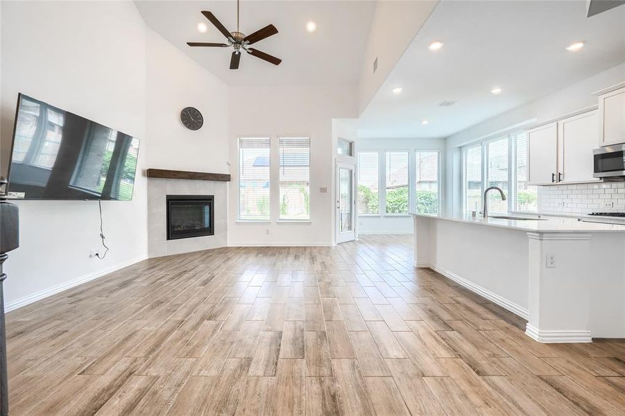 Unfurnished living room with wood tiled floors, a tiled fireplace, recessed lighting, a ceiling fan, and a high ceiling Unfurnished living room with wood tiled floors, a tiled fireplace, recessed lighting, a ceiling fan, and a high ceiling