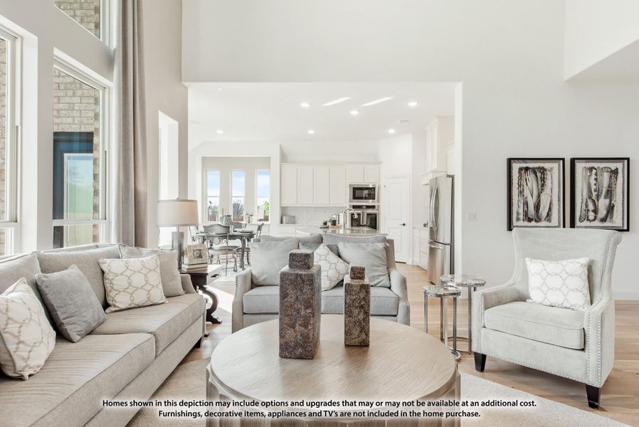 Open-concept living room with high ceilings, gray sofas, and kitchen visible in background on hardwood floors