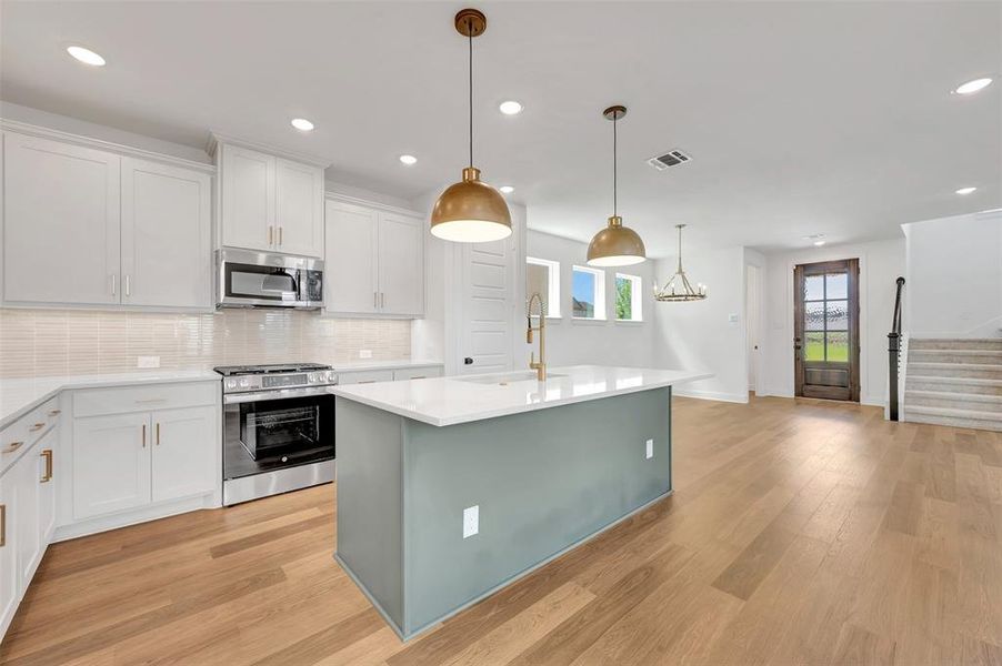Modern kitchen featuring a central island with a light teal base, white countertops, stainless steel appliances, white cabinetry, and wood-finish flooring