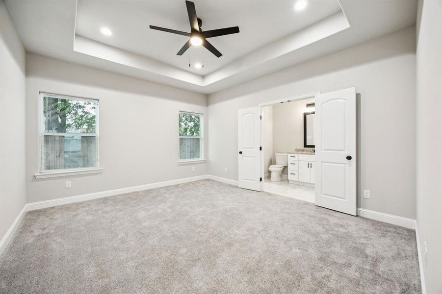 (Bedroom #1) Master bedroom featuring light carpet, a ceiling fan, a tray ceiling, ensuite bath, and recessed lighting