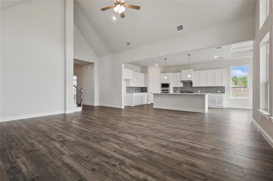 Unfurnished living room with a ceiling fan, visible vents, baseboards, and dark wood finished floors