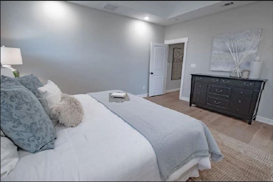 Spacious room featuring light gray walls, wood-finish flooring, a tray ceiling with recessed lighting, and a white paneled door with black hardware