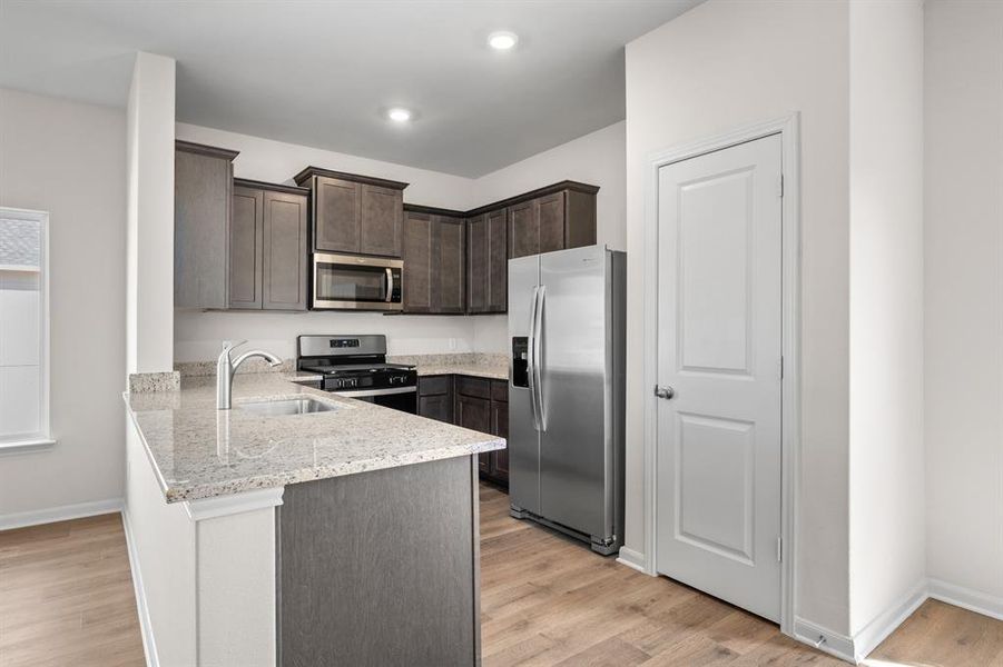Kitchen with stainless steel appliances, dark brown cabinets, light stone counters, a peninsula, and light wood finished floors