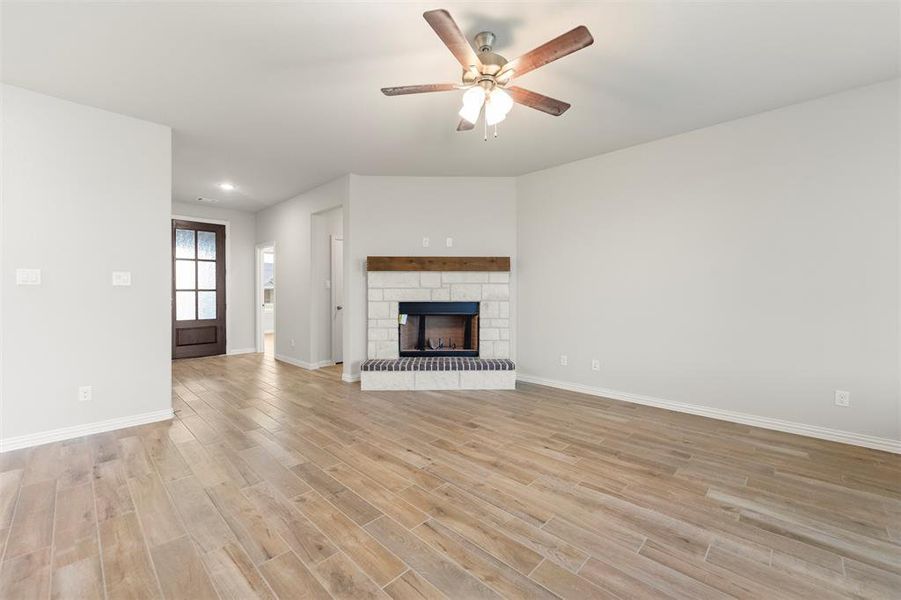 Unfurnished living room with light wood-type flooring, a stone fireplace, and a ceiling fan Unfurnished living room with light wood-type flooring, a stone fireplace, and a ceiling fan