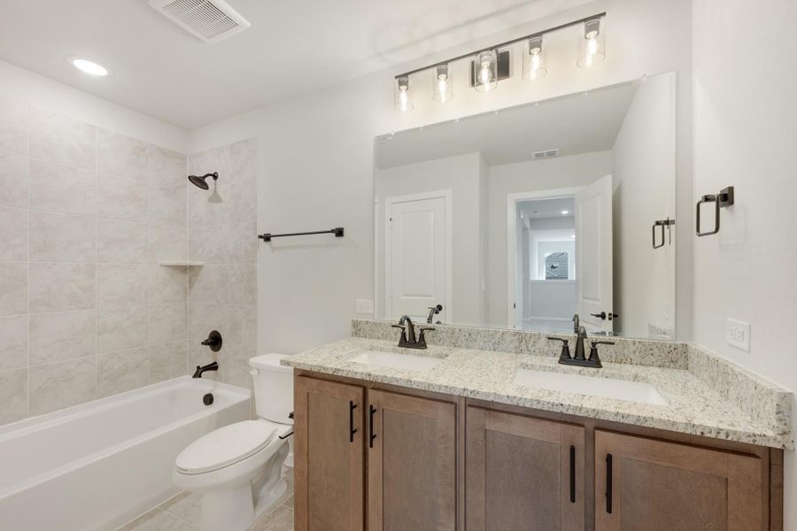 Bathroom with double sink vanity, granite countertop, tiled shower-tub combo, and large mirror with overhead lighting Bathroom with double sink vanity, granite countertop, tiled shower-tub combo, and large mirror with overhead lighting