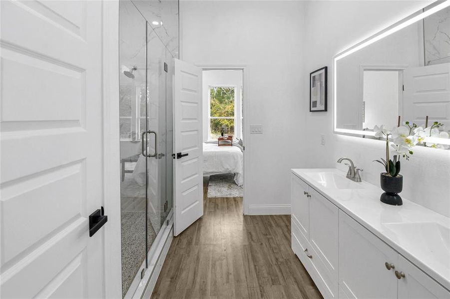 Ensuite bathroom featuring dark wood-style floors, double vanity, and a marble finish shower Ensuite bathroom featuring dark wood-style floors, double vanity, and a marble finish shower