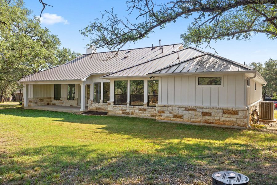 Back of house with a patio, stone siding, a lawn, a metal roof, and board and batten siding