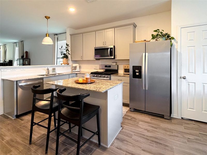 Kitchen featuring appliances with stainless steel finishes, a center island, light stone countertops, pendant lighting, and a breakfast bar Kitchen featuring appliances with stainless steel finishes, a center island, light stone countertops, pendant lighting, and a breakfast bar