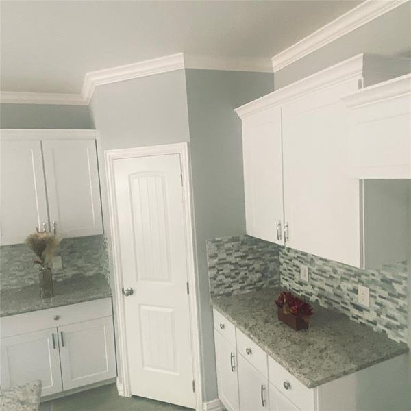 Kitchen featuring white cabinets, tasteful backsplash, crown molding, and light stone countertops Kitchen featuring white cabinets, tasteful backsplash, crown molding, and light stone countertops
