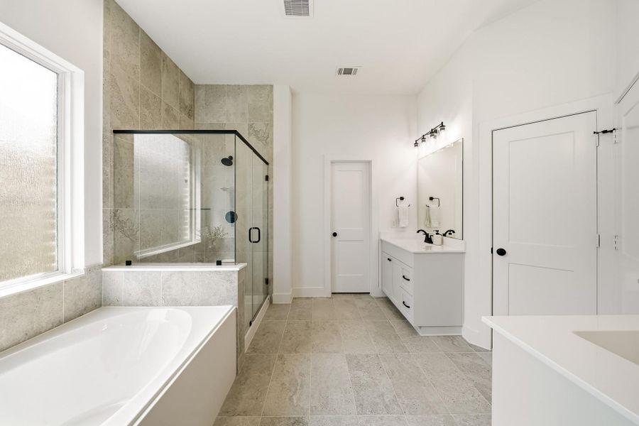 Double doors lead to a beautifully appointed primary bath, where wood-like tile flooring sets a warm, refined tone. Dual quartz-topped vanities offer both style and functionality, while decorative fixtures and recessed lighting create a layered, sophisticated ambiance throughout the space.